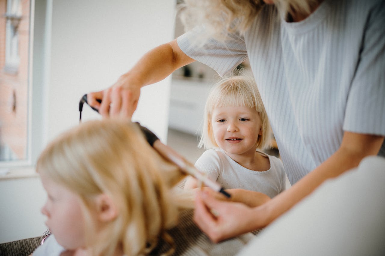 A woman styling her child's hair with a curling iron, creating a warm family bonding moment.